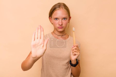 Téléchargez les photos : Caucasien adolescent fille brossage dents isolé sur beige fond debout avec tendu main montrant stop signe, vous empêchant. - en image libre de droit