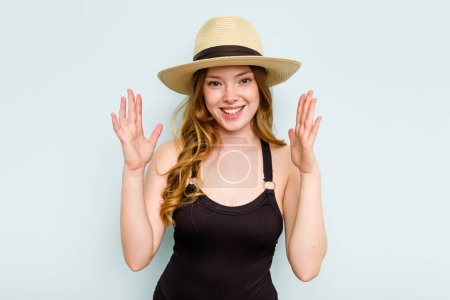 Photo for Young caucasian woman going to the beach isolated on blue background receiving a pleasant surprise, excited and raising hands. - Royalty Free Image