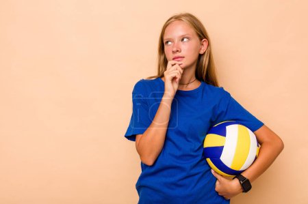 Téléchargez les photos : Petite fille caucasienne jouant au volley isolé sur fond beige regardant de côté avec une expression douteuse et sceptique. - en image libre de droit