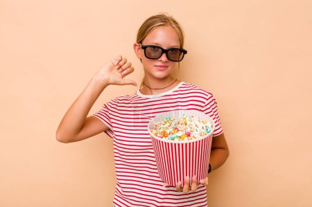 Photo for Little caucasian girl eating popcorn isolated on beige background feels proud and self confident, example to follow. - Royalty Free Image