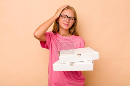 Foto de Pequeña chica caucásica sosteniendo pizza aislada sobre fondo beige siendo sorprendida, ella ha recordado importante reunión. - Imagen libre de derechos