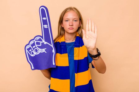 Téléchargez les photos : Petite fille fan de sport caucasienne isolée sur fond beige debout avec la main tendue montrant le signe d'arrêt, vous empêchant. - en image libre de droit