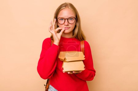 Téléchargez les photos : Petite étudiante caucasienne tenant des hamburgers isolés sur fond beige avec les doigts sur les lèvres gardant un secret. - en image libre de droit