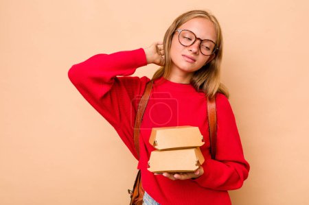 Téléchargez les photos : Petite étudiante caucasienne tenant des hamburgers isolés sur fond beige touchant l'arrière de la tête, pensant et faisant un choix. - en image libre de droit