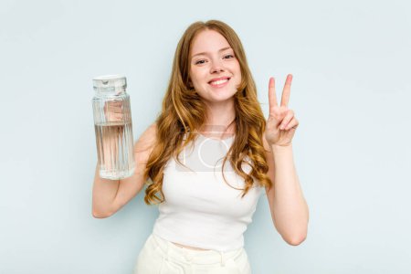 Foto de Joven mujer caucásica sosteniendo tarro de agua aislada sobre fondo azul mostrando el número dos con los dedos. - Imagen libre de derechos