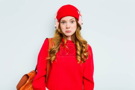 Téléchargez les photos : Jeune étudiante femme portant des écouteurs isolés sur fond bleu haussant les épaules et les yeux ouverts confus. - en image libre de droit