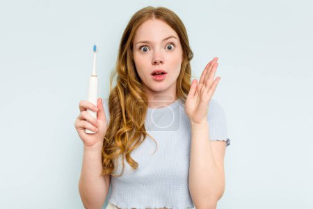 Téléchargez les photos : Jeune femme caucasienne tenant une brosse à dents électrique isolée sur fond bleu surprise et choquée. - en image libre de droit
