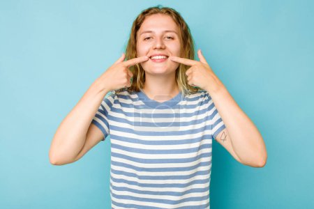 Téléchargez les photos : Jeune femme caucasienne isolée sur fond bleu sourit, pointant les doigts vers la bouche. - en image libre de droit