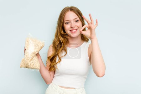 Photo for Young caucasian woman holding oatmeal isolated on blue background cheerful and confident showing ok gesture. - Royalty Free Image