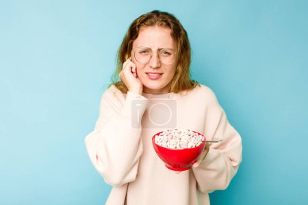 Photo for Young caucasian woman holding a bowl of cereals isolated on blue background covering ears with hands. - Royalty Free Image