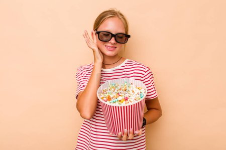 Photo for Little caucasian girl eating popcorn isolated on beige background covering ears with hands. - Royalty Free Image