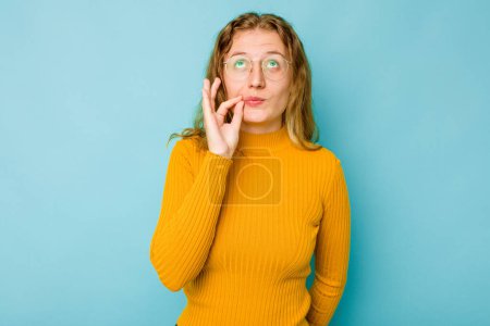 Téléchargez les photos : Jeune femme caucasienne isolée sur fond bleu avec les doigts sur les lèvres gardant un secret. - en image libre de droit