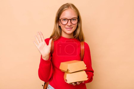 Téléchargez les photos : Petite étudiante caucasienne tenant des hamburgers isolés sur fond beige souriant gai montrant numéro cinq avec les doigts. - en image libre de droit
