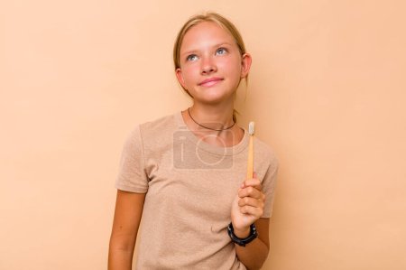 Téléchargez les photos : Caucasien adolescent fille brossage dents isolé sur fond beige rêve d'atteindre des objectifs et des objectifs - en image libre de droit