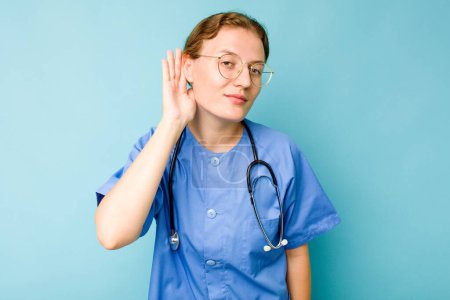 Foto de Joven enfermera caucásica aislada sobre fondo azul tratando de escuchar un chisme. - Imagen libre de derechos