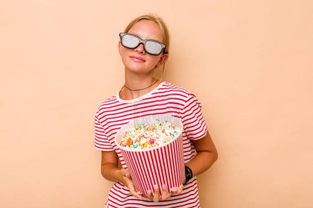 Photo for Little caucasian girl eating popcorn isolated on beige background dreaming of achieving goals and purposes - Royalty Free Image