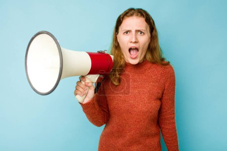 Téléchargez les photos : Jeune femme caucasienne tenant mégaphone isolé sur fond bleu criant très en colère et agressif. - en image libre de droit