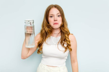 Photo for Young caucasian woman holding jar of water isolated on blue background shrugs shoulders and open eyes confused. - Royalty Free Image