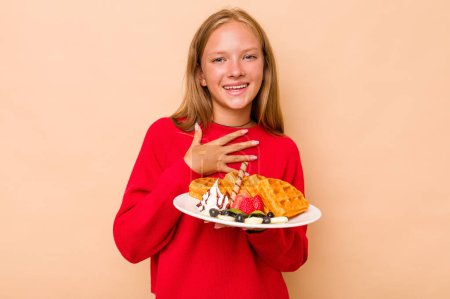 Photo for Little caucasian girl holding a waffles isolated on beige background laughs out loudly keeping hand on chest. - Royalty Free Image