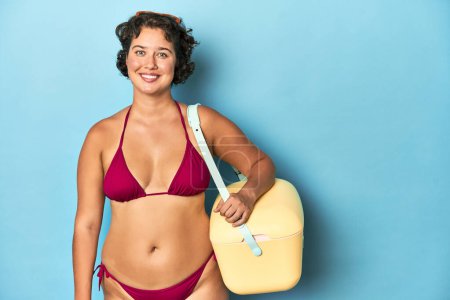 Foto de Joven mujer caucásica en bikini sosteniendo un enfriador de playa, toma de estudio. - Imagen libre de derechos