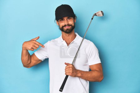 Foto de Golfista de pelo largo con club y sombrero persona señalando a mano a un espacio de copia de la camisa, orgulloso y seguro - Imagen libre de derechos