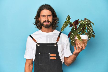 Téléchargez les photos : Jardinier aux cheveux longs avec barbe tenant une plante criant très en colère et agressif. - en image libre de droit