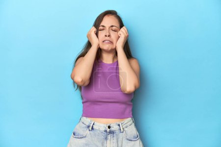 Foto de Mujer joven de moda en un top púrpura sobre fondo azul llorando, infeliz con algo, agonía y concepto de confusión. - Imagen libre de derechos