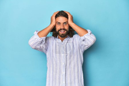 Photo for Man with beard in blue striped shirt, blue studio screaming, very excited, passionate, satisfied with something. - Royalty Free Image