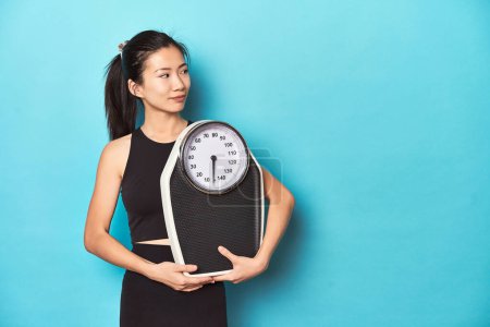 Photo for Asian sportswoman holding scale, studio shot. - Royalty Free Image