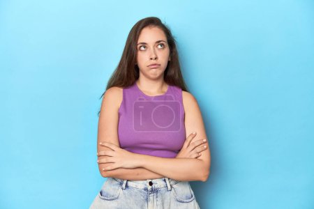 Photo for Fashionable young woman in a purple top on blue background tired of a repetitive task. - Royalty Free Image