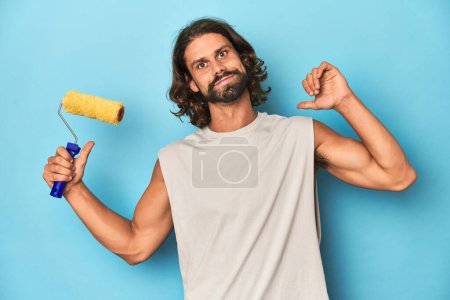 Foto de El hombre barbudo pintando con un rodillo amarillo se siente orgulloso y seguro de sí mismo, ejemplo a seguir. - Imagen libre de derechos