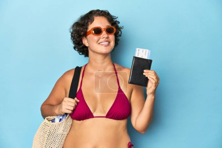 Photo for Young Caucasian woman in bikini with beach bag and airplane ticket, studio shot. - Royalty Free Image