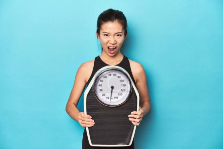 Photo for Asian sportswoman holding scale, shouting to camera. - Royalty Free Image