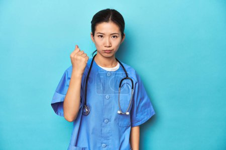 Photo for Asian nurse with stethoscope, medical studio shot, showing fist to camera, aggressive facial expression. - Royalty Free Image