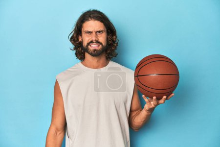 Téléchargez les photos : Homme barbu avec basket en studio bleu criant très en colère et agressif. - en image libre de droit