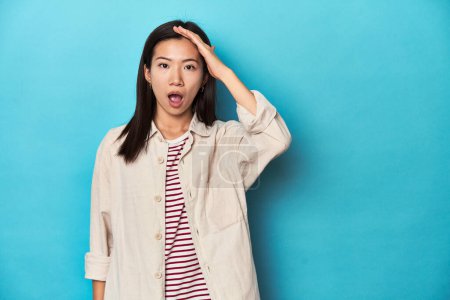 Téléchargez les photos : Femme asiatique en chemise à couches et t-shirt rayé, crie fort, garde les yeux ouverts et les mains tendues. - en image libre de droit
