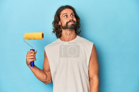 Téléchargez les photos : Peinture homme barbu avec un rouleau jaune rêvant d'atteindre les objectifs et les buts - en image libre de droit