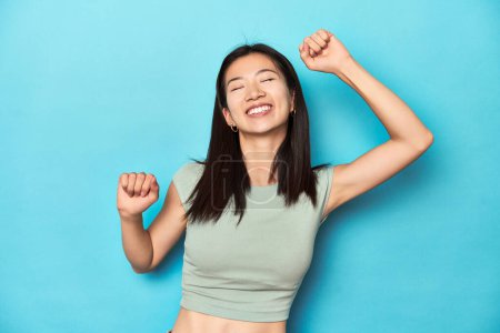 Photo for Asian woman in summer green top, studio backdrop, celebrating a special day, jumps and raise arms with energy. - Royalty Free Image