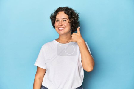Foto de Mujer joven caucásica con el pelo corto mostrando un gesto de llamada de teléfono móvil con los dedos. - Imagen libre de derechos