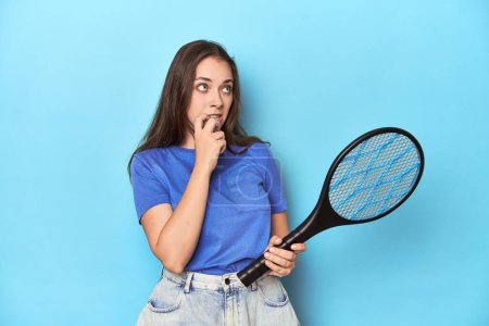 Photo for Woman with an electric bug zapper on a blue background relaxed thinking about something looking at a copy space. - Royalty Free Image