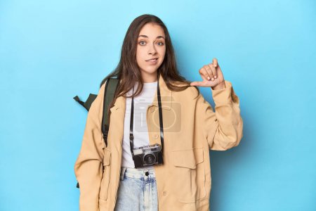 Téléchargez les photos : Jeune voyageuse caucasienne avec caméra et sac à dos montrant un geste détestable, pouces baissés. Concept de désaccord. - en image libre de droit