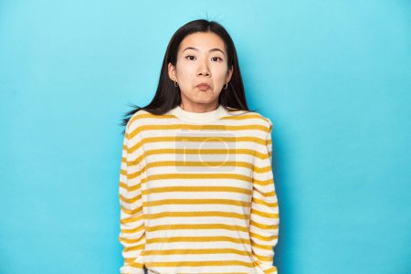 Photo for Asian woman in striped yellow sweater, shrugs shoulders and open eyes confused. - Royalty Free Image