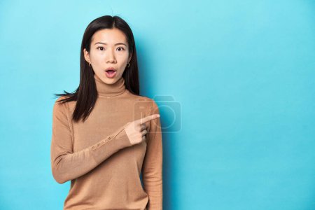 Photo for Young Asian woman in brown turtleneck, pointing to the side - Royalty Free Image