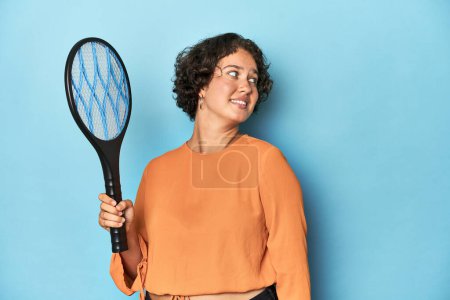 Photo for Young woman with electric mosquito racket Young woman with electric mosquito racketlooks aside smiling, cheerful and pleasant. - Royalty Free Image