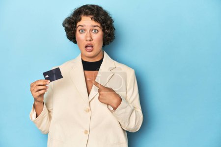 Téléchargez les photos : Jeune femme avec carte de crédit, élégant blazer blanc pointant vers le côté - en image libre de droit
