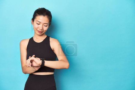 Photo for Asian sportswoman setting smartwatch before activity. - Royalty Free Image