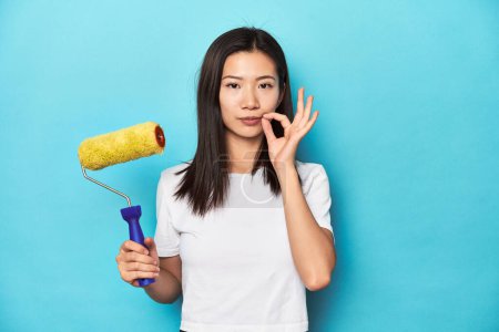 Téléchargez les photos : Jeune femme asiatique avec rouleau de peinture, concept de bricolage, avec les doigts sur les lèvres gardant un secret. - en image libre de droit