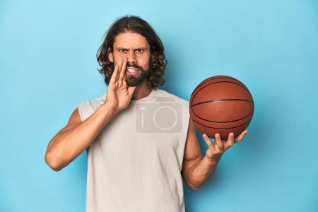 Photo for Bearded man with basketball in blue studio is saying a secret hot braking news and looking aside - Royalty Free Image