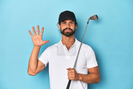 Téléchargez les photos : Golfeur aux cheveux longs avec club et chapeau souriant gai montrant numéro cinq avec les doigts. - en image libre de droit