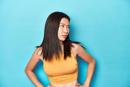 Foto de Mujer asiática en la parte superior amarilla de verano, configuración del estudio, confundido, se siente dudoso e inseguro. - Imagen libre de derechos